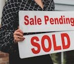 A businesswoman holding 'Sale Pending' and 'Sold' signs indicating a successful real estate transaction.