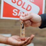 Hands exchanging house keys in front of a sold sign, symbolizing real estate success.